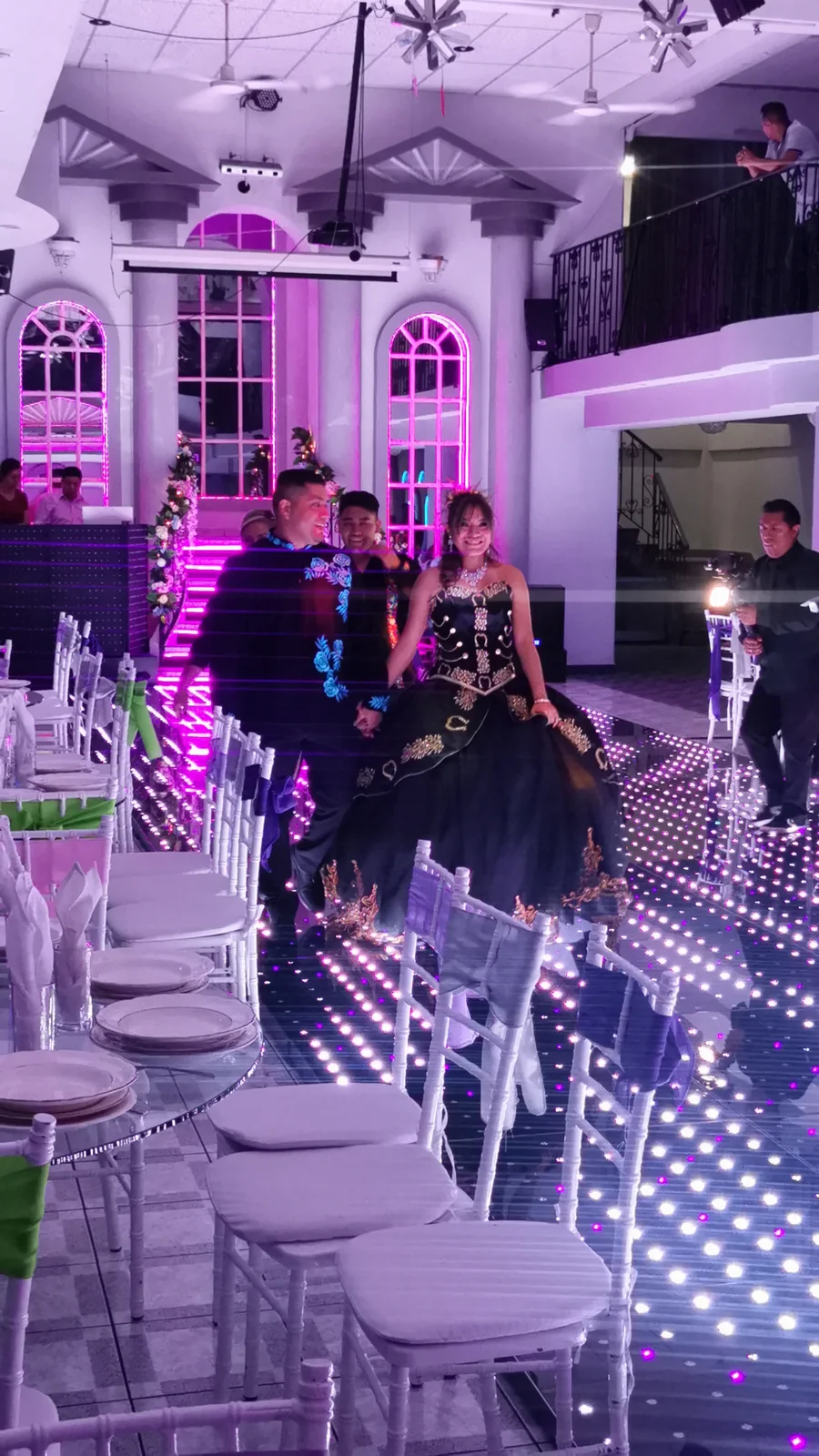 Quinceañera con vestido negro entrando al salón por una pista iluminada