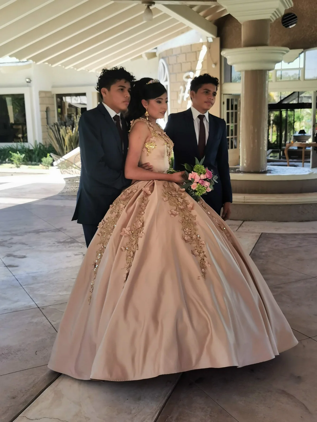 Quinceañera con vestido color champagne acompañada por sus chambelanes