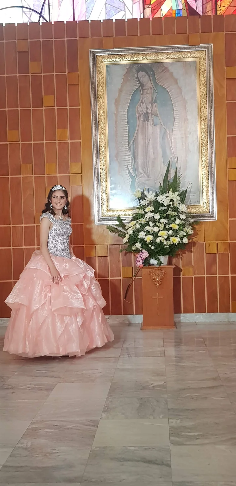 Quinceañera con vestido rosa junto a una imagen de la Virgen de Guadalupe